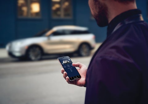 A person is shown interacting with a smartphone to connect to a Lincoln vehicle across the street. | Doral Lincoln in Doral FL