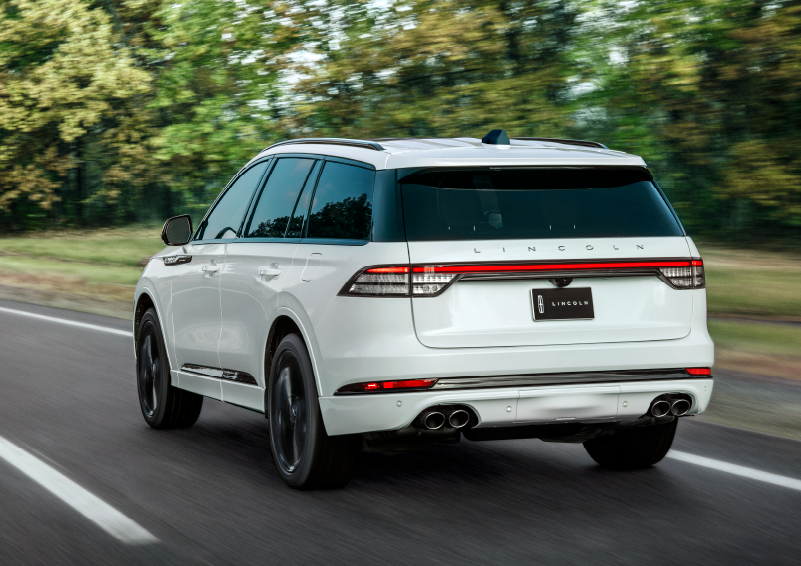 A white 2025 Lincoln Aviator® SUV is being driven away down a road lined with colorful trees. | Doral Lincoln in Doral FL