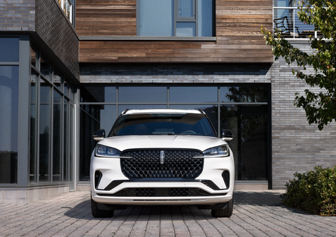A white 2025 Lincoln Aviator® SUV is shown parked outside a modern building with gray brick and wood accents. | Doral Lincoln in Doral FL