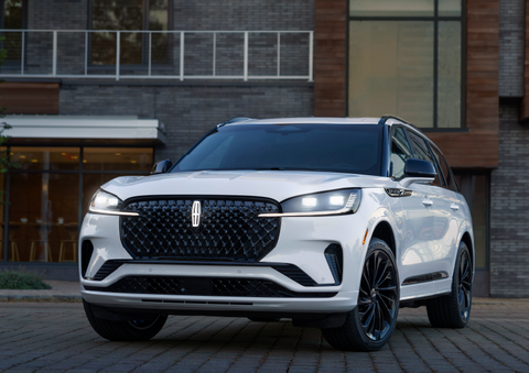 A white 2025 Lincoln Aviator® SUV is shown parked outside a modern building with gray brick and wood accents. | Doral Lincoln in Doral FL