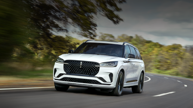 A white 2025 Lincoln Aviator® SUV is being driven down a road lined with trees. | Doral Lincoln in Doral FL